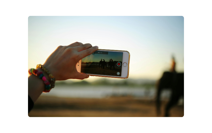 Close-up of a hand holding a smartphone recording a video of horses at sunset, demonstrating faceless content creation.